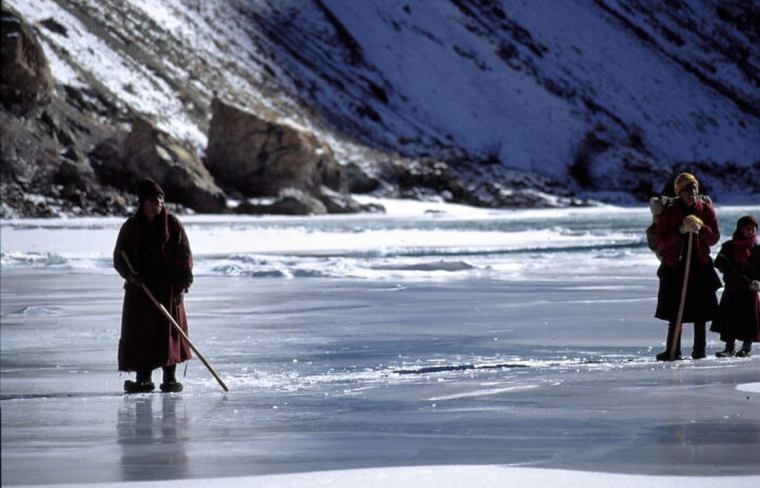 Trekkers walking on the frozen Zanskar River during the Chadar Trek, surrounded by steep icy cliffs and snow-covered terrain in Ladakh