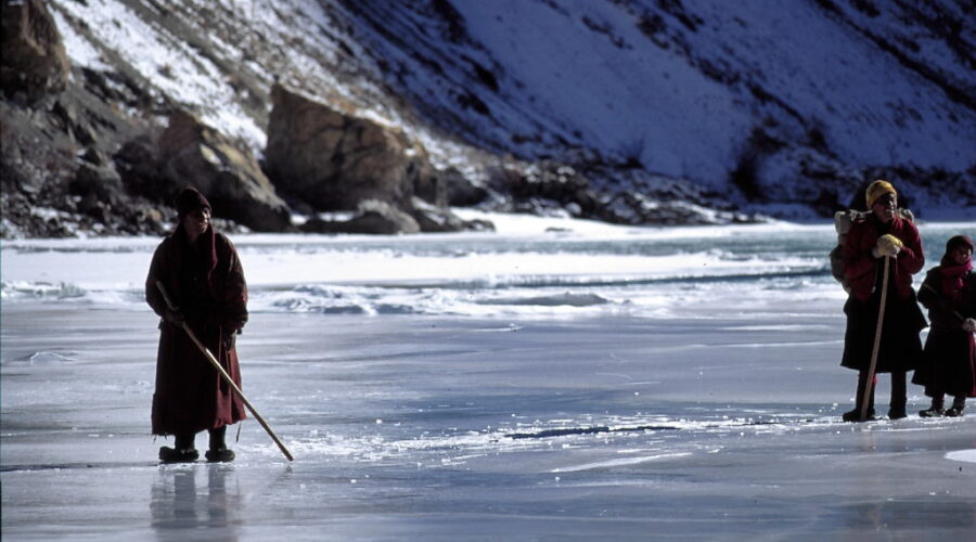 Trekkers walking on the frozen Zanskar River during the Chadar Trek, surrounded by steep icy cliffs and snow-covered terrain in Ladakh