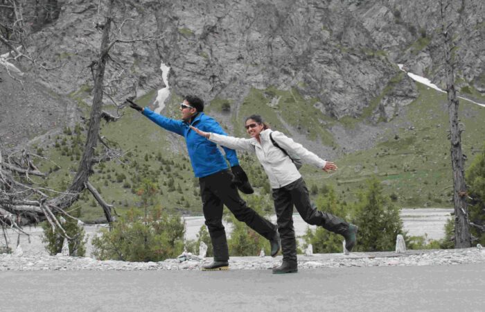 A happy couple posing playfully beside a mountain road during Into Wild Himalaya’s Foothills of the Himalayas Motorcycle Tour, showing the joy and freedom of riding through the Himalayas.