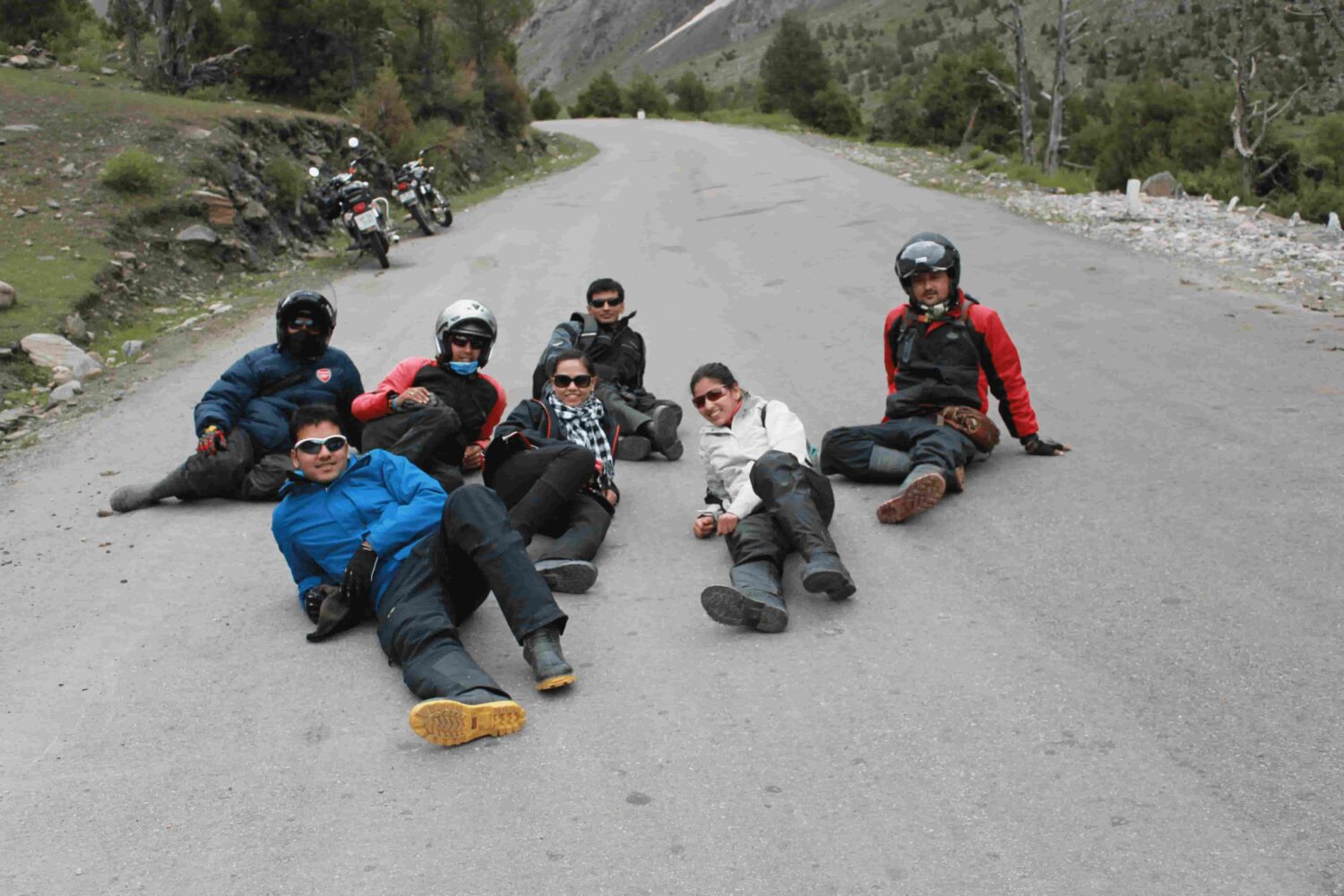 A group of motorcycle riders relaxing on a mountain road during Into Wild Himalaya’s Foothills of the Himalayas Motorcycle Tour in Himachal Pradesh, India.
