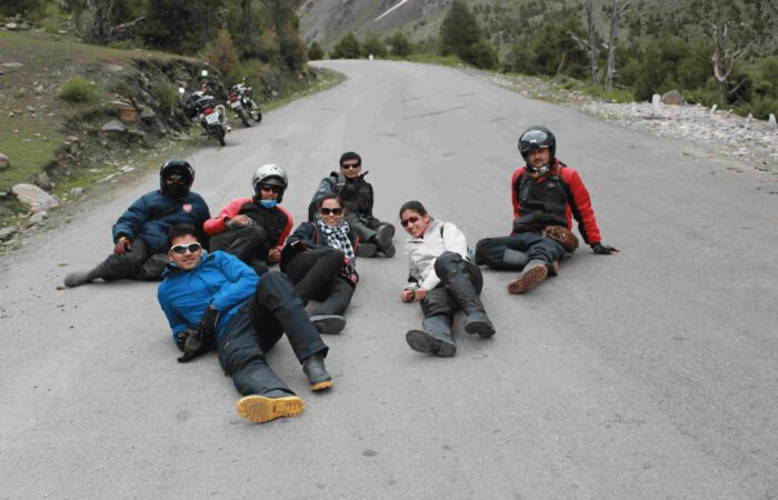 A group of motorcycle riders relaxing on a mountain road during Into Wild Himalaya’s Foothills of the Himalayas Motorcycle Tour in Himachal Pradesh, India.
