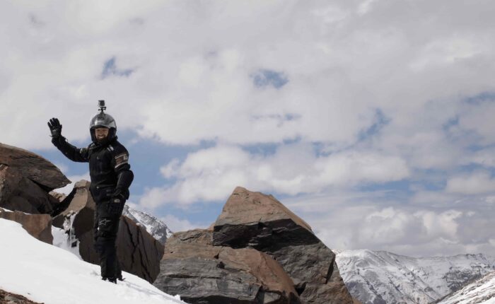 Alan from Australia walking on snow-covered mountain waving to fellow riders during the Royal Enfield Motorcycle Tour with Into Wild Himalaya