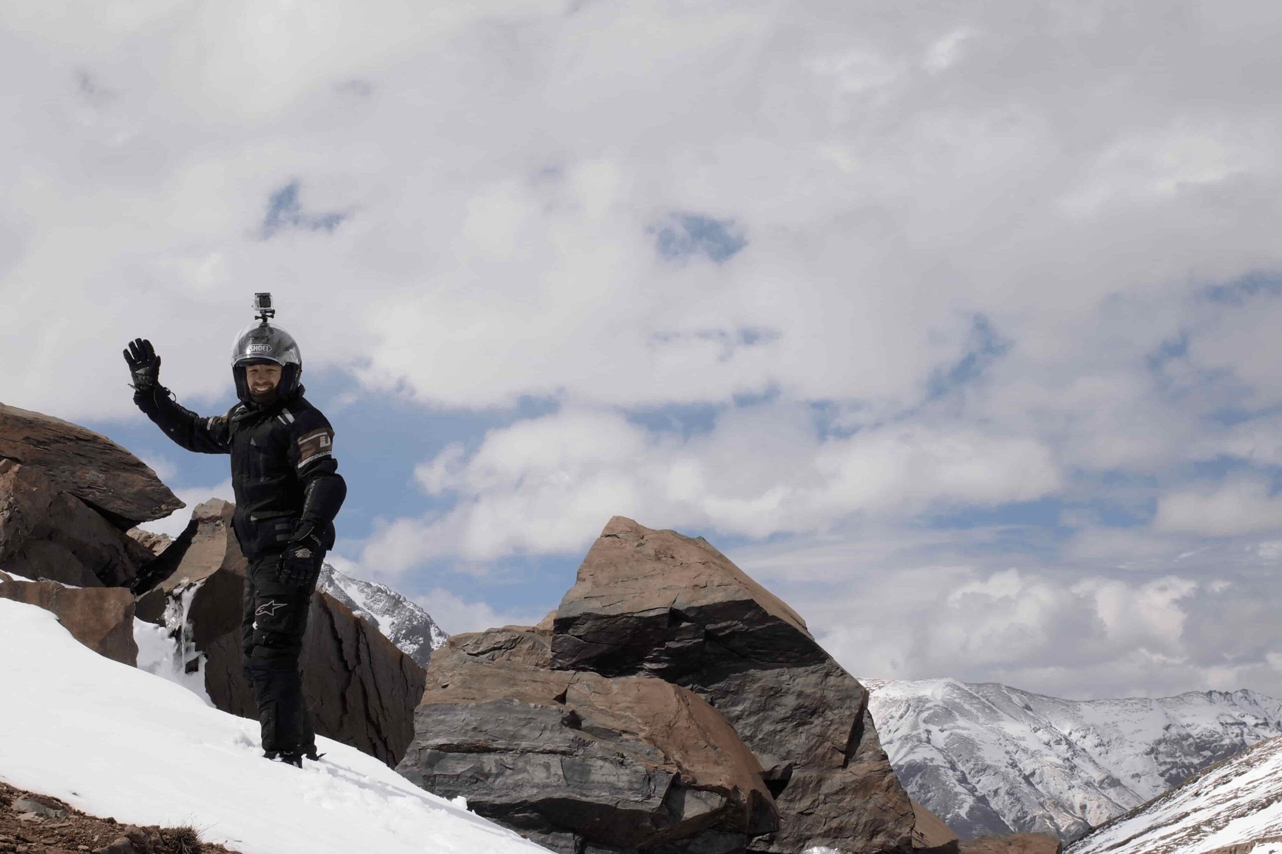Alan from Australia walking on snow-covered mountain waving to fellow riders during the Royal Enfield Motorcycle Tour with Into Wild Himalaya