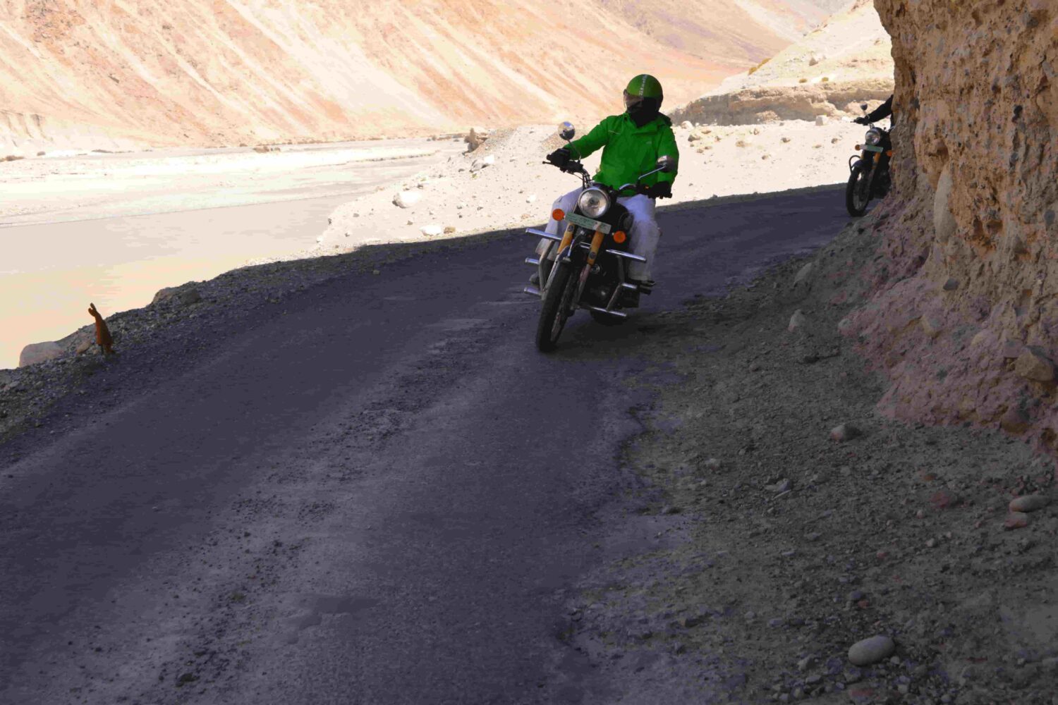 Riders on Royal Enfield motorcycles crossing a mountain bridge in the foothills of the Himalayas during Into Wild Himalaya’s guided adventure tour in North India.