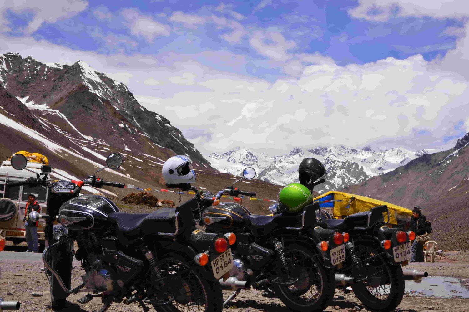 Motorcycles parked with helmets on mirrors as bikers admire snow-covered Himalayan mountains on the Manali to Leh route