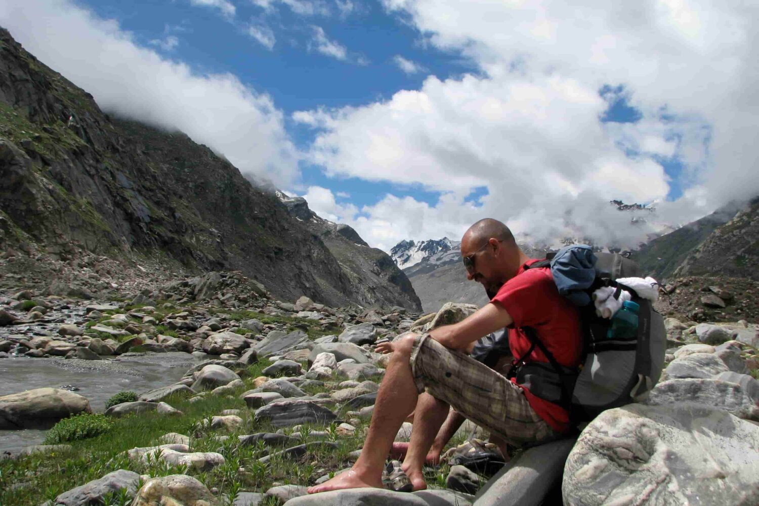 Trekker resting beside a rocky river valley during the Pin Parvati Pass Trek in the Himalayas.