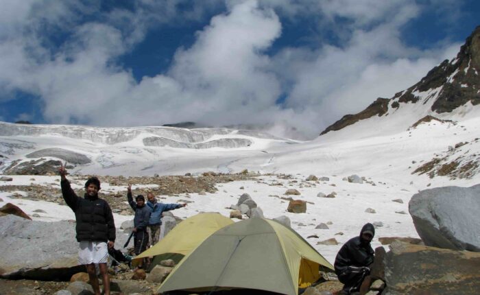 Trekkers at a high-altitude campsite on the Pin Parvati Pass Trek in the Himalayas with snow, mountains, and tents.