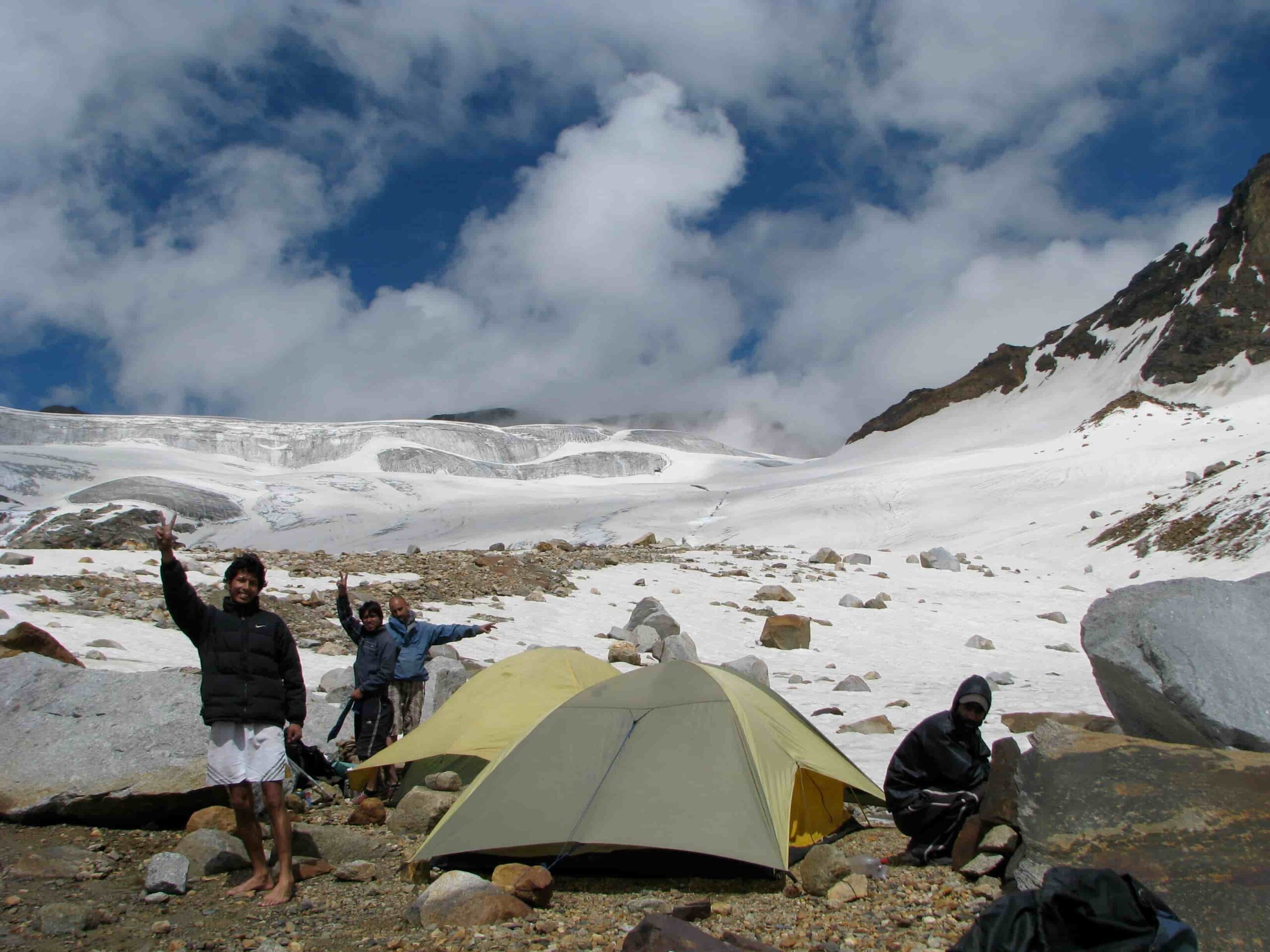 Trekkers at a high-altitude campsite on the Pin Parvati Pass Trek in the Himalayas with snow, mountains, and tents.