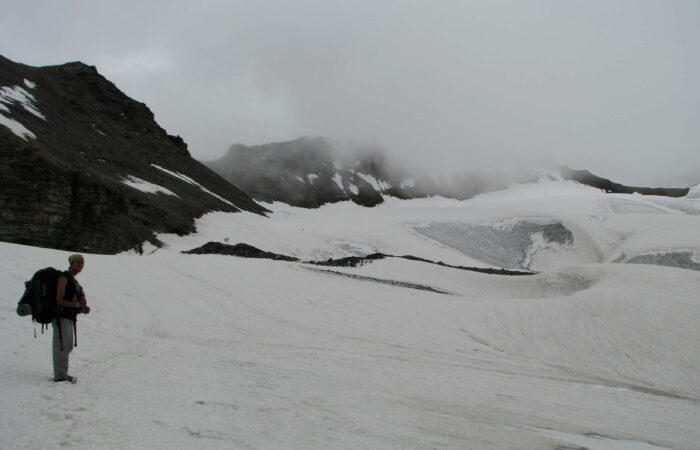 Trekker walking across a snowy glacier during the Pin Parvati Pass Trek in the Himalayas.