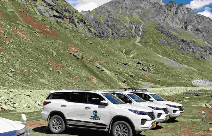 White 4x4 vehicles on a high-altitude Himalayan road with mountains, clear blue sky, and rugged terrain during a guided road trip in India.
