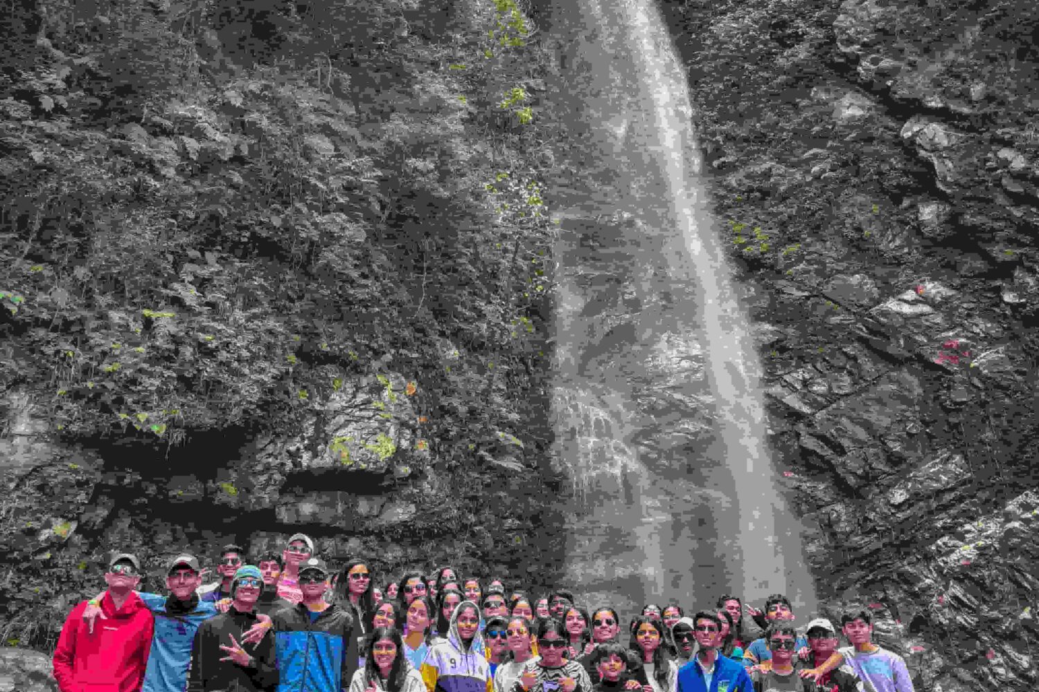 A group of campers posing in front of a tall waterfall during a weekend camping trip in Tirthan Valley, India.