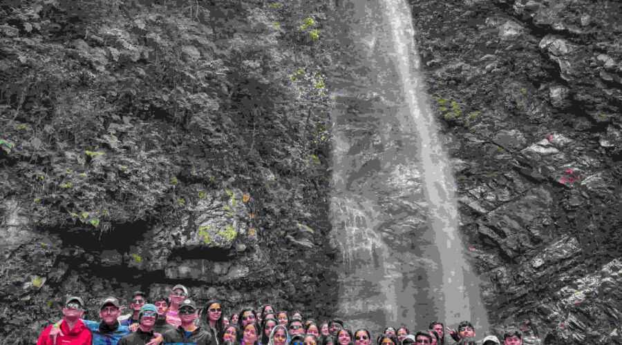 A group of campers posing in front of a tall waterfall during a weekend camping trip in Tirthan Valley, India.
