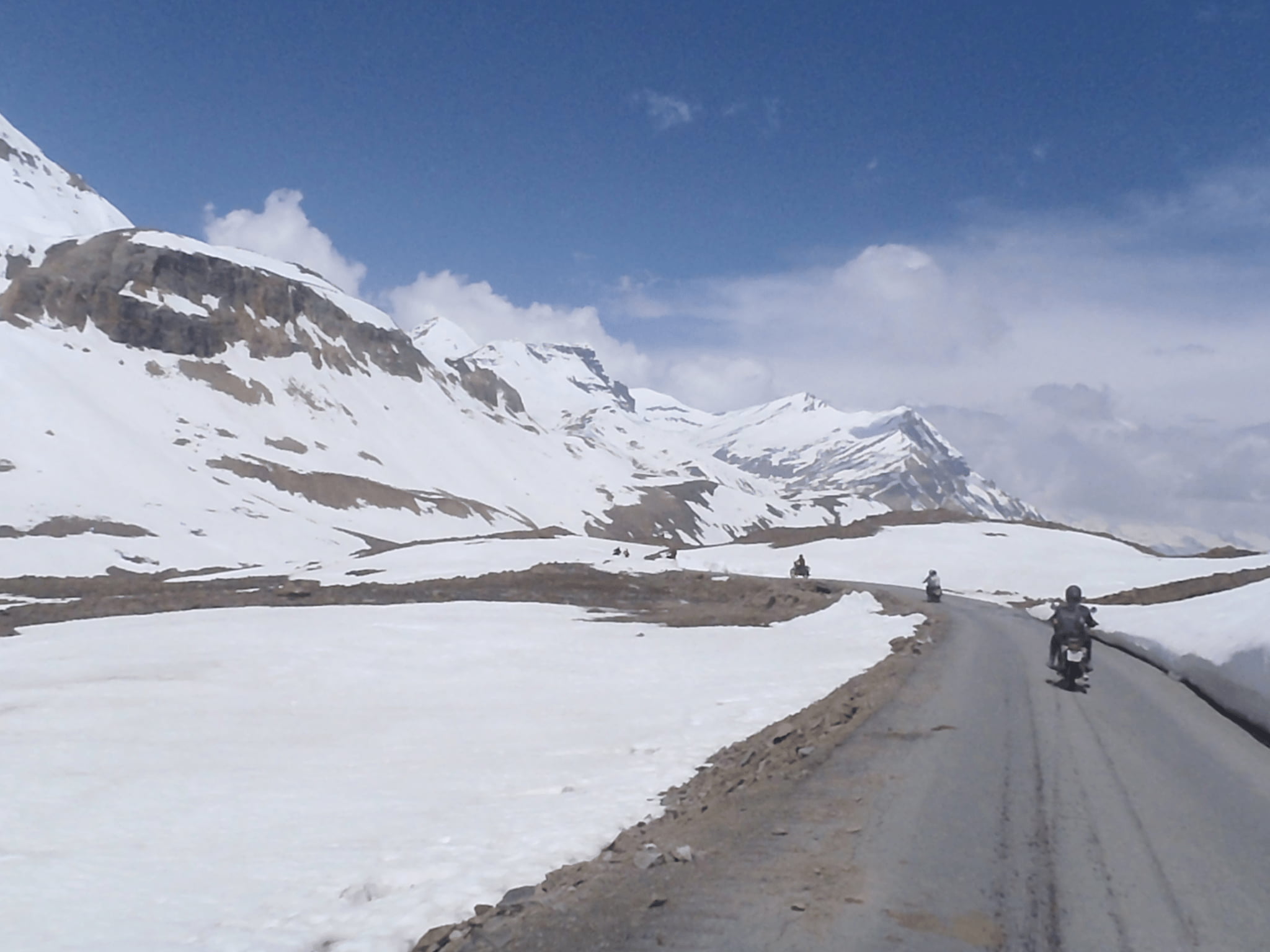 Riders on motorcycles crossing a snow-covered mountain pass during a motorcycle expedition in the Himalayas.