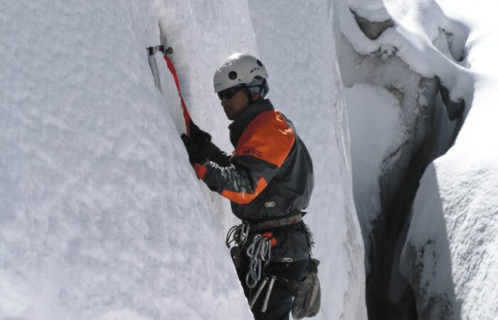 Trainee practicing vertical ice climbing with ice axes and crampons during the Private Basic Mountaineering Course in Manali India on a steep Himalayan ice wall.