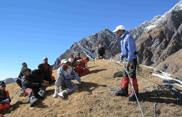 Instructor demonstrating anchor building and rope safety techniques to students during the Private Basic Mountaineering Course in Manali India, with Himalayan peaks in the background.