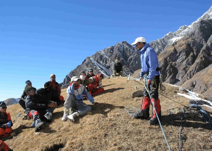 Instructor demonstrating anchor building and rope safety techniques to students during the Private Basic Mountaineering Course in Manali India, with Himalayan peaks in the background.